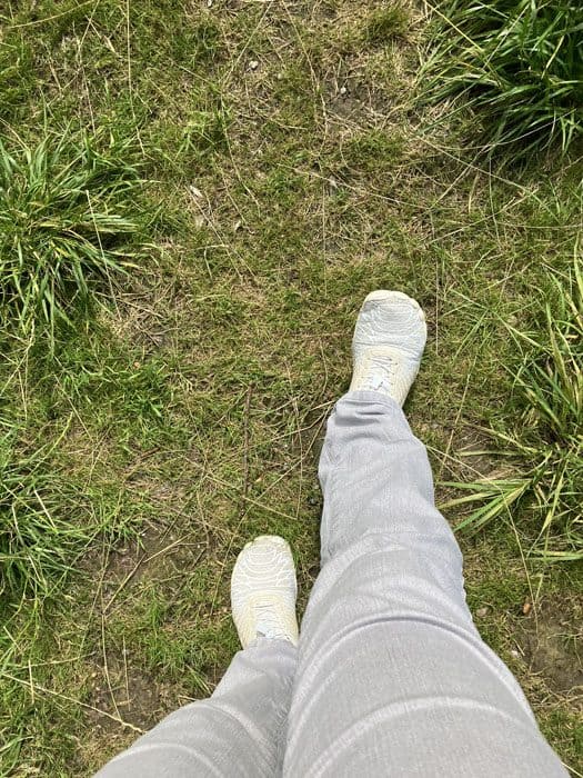 Blick von oben auf die eigenen Füße in weißen Schuhen auf einem schmalen Graspfad, der erste Schritt nach draußen in einem Moment, in dem man sich eigentlich nicht aufraffen kann