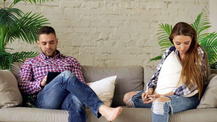 Paar sitzt einsam trotz Social Media nebeneinander auf dem Sofa, beide blicken aufs Handy