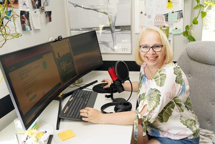 Alwina Simon, Life Coach für digitale Balance, sitzt lächelnd an ihrem Schreibtisch vor einem Podcast-Mikrofon, auf dem Monitor ihre Website mit dem Workbook Bewusst Offline!.