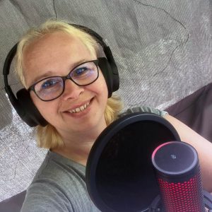 Alwina Simon, Life Coach für digitale Balance, sitzt lächelnd in ihrem Gartenstudio vor einem Podcast-Mikrofon.