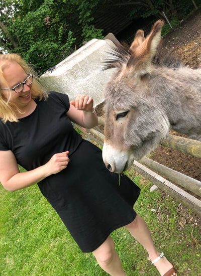 Momentaufnahme: Links im Bild ist Alwina Simon in einem schwarzen Kleid zu sehen. Sie streichelt einen Esel und freut sich über dessen sehr weiches Fell. Das Bild stammt aus dem Jahr 2022 und ist Teil des privaten Bildarchivs von Alwina Simon.