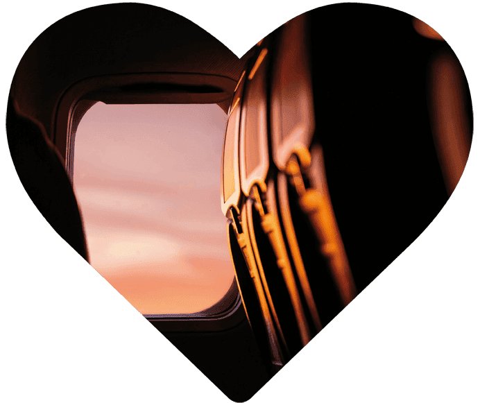 Blick aus dem Fenster eines Passagierflugzeugs auf einen Himmel in Sonnenuntergangsfarben, herzförmig zugeschnitten.